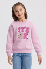 Polerón rosa para niña con diseño de "IT'S OK" en el frente letras grandes con carita feliz y flores estilo gráfico