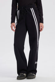 Pantalón buzo niña negro con corte wide leg líneas blancas verticales a los lados diseño deportivo y texto "active" en el tobillo