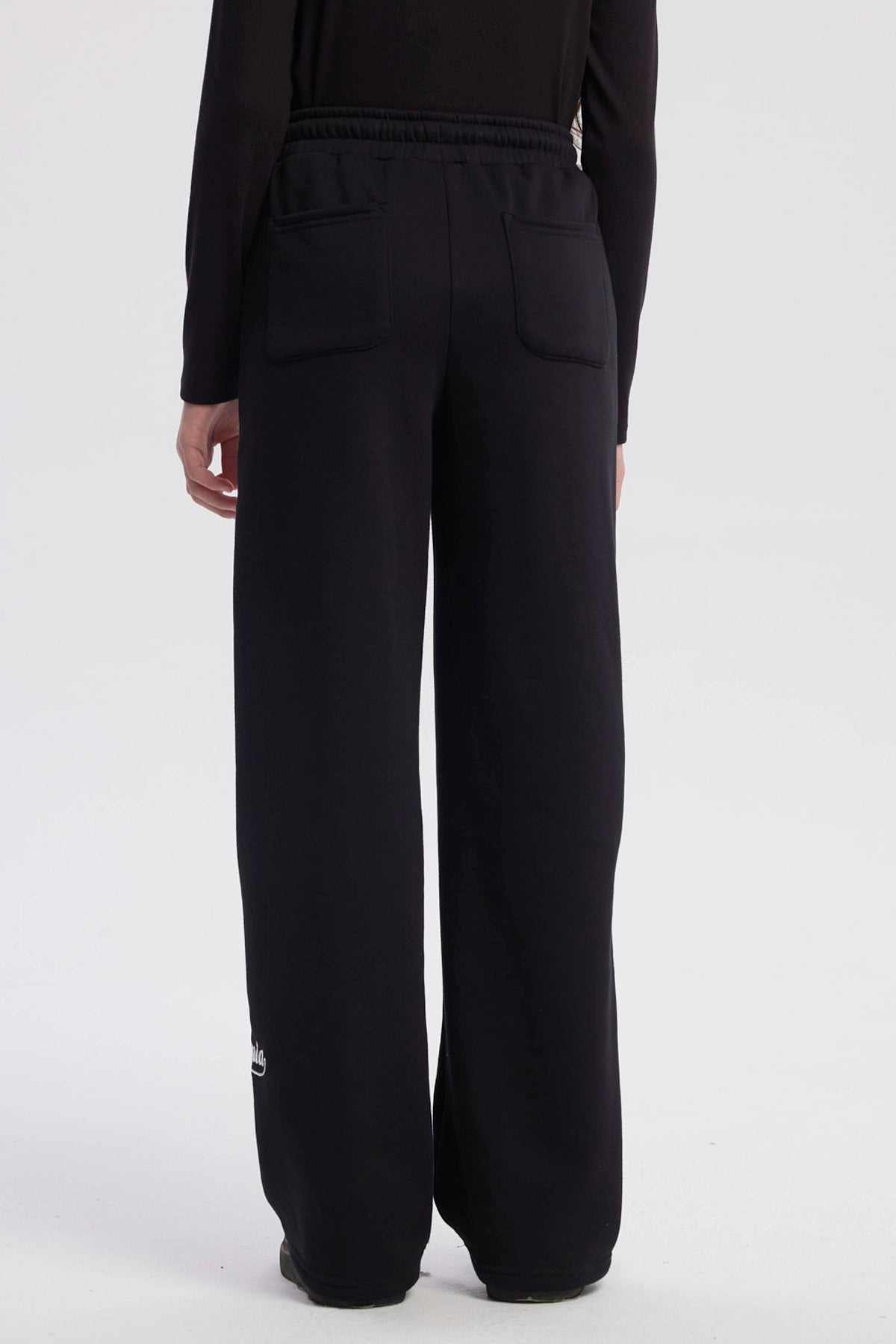 Pantalón buzo niña negro con corte wide leg líneas blancas verticales a los lados diseño deportivo y texto "active" en el tobillo
