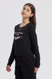 Polera negra de niña con argollas en el cuello y estampado frontal New York en letras blancas y rojas estilo urbano
