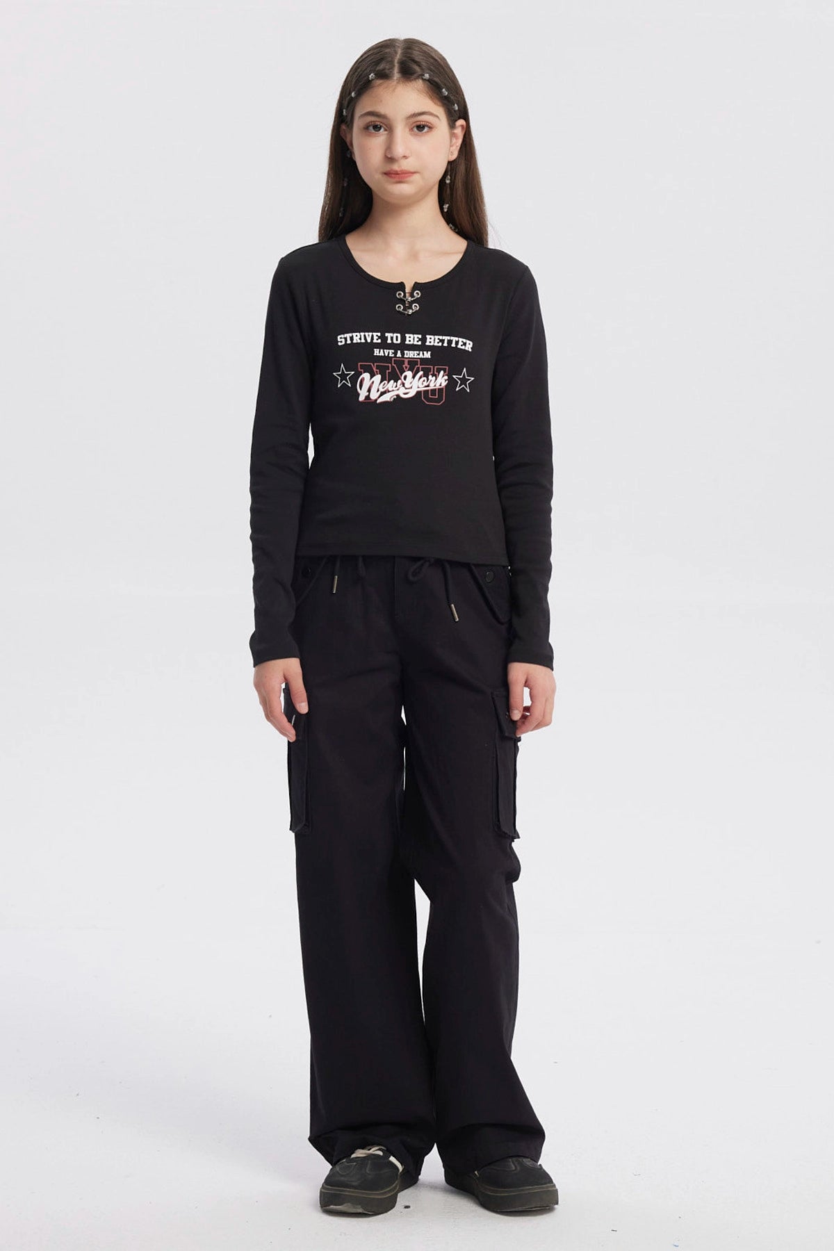 Polera negra de niña con argollas en el cuello y estampado frontal New York en letras blancas y rojas estilo urbano