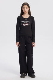 Polera negra de niña con argollas en el cuello y estampado frontal New York en letras blancas y rojas estilo urbano