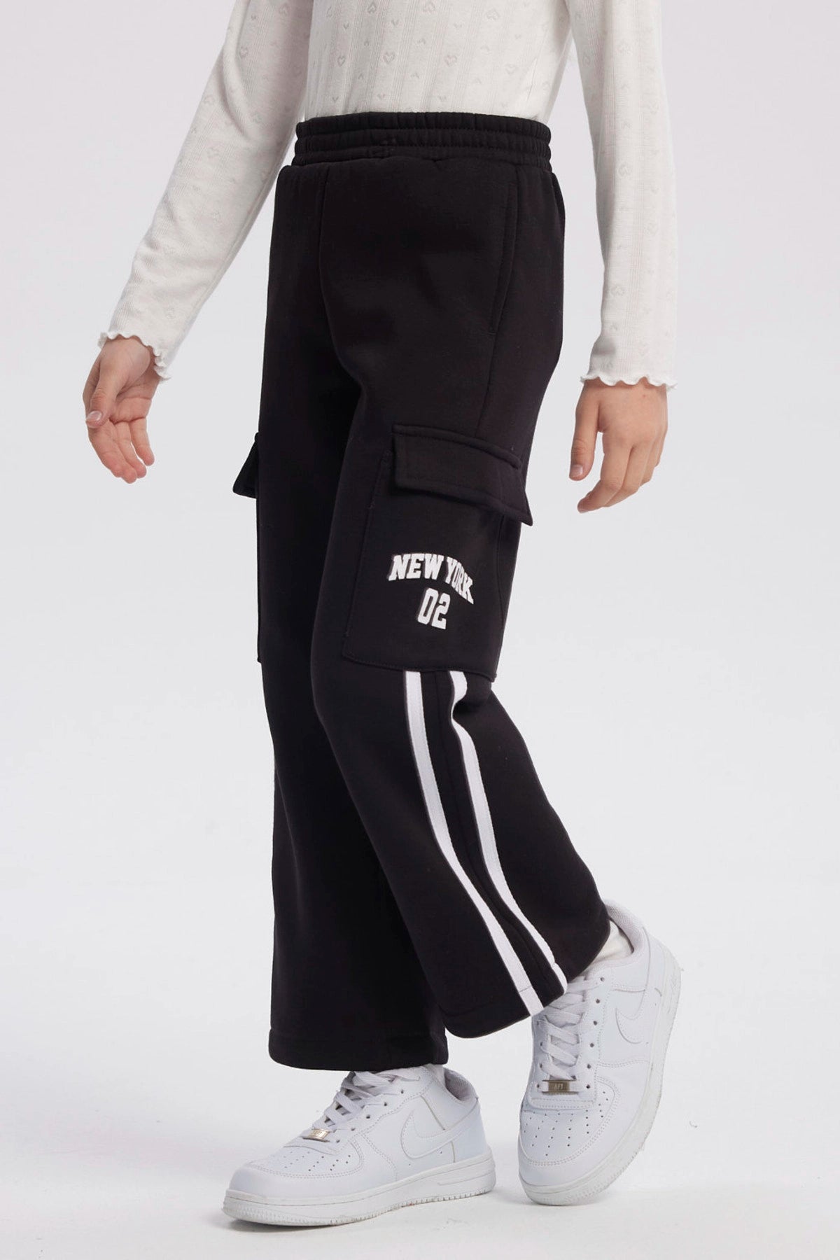 Pantalón buzo negro niña con bolsillo lateral y texto New York Dreams en la pierna estilo casual relajado