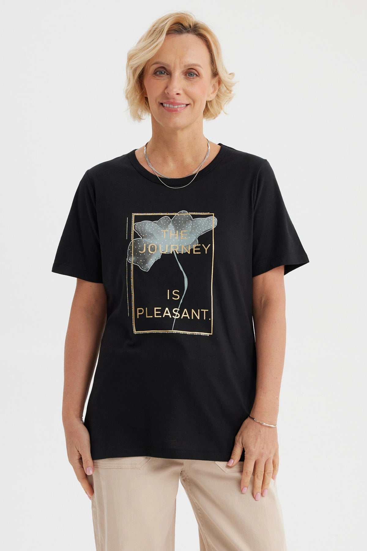 Polera negra mujer con estampado frontal de flor y texto The journey is pleasant en letras doradas