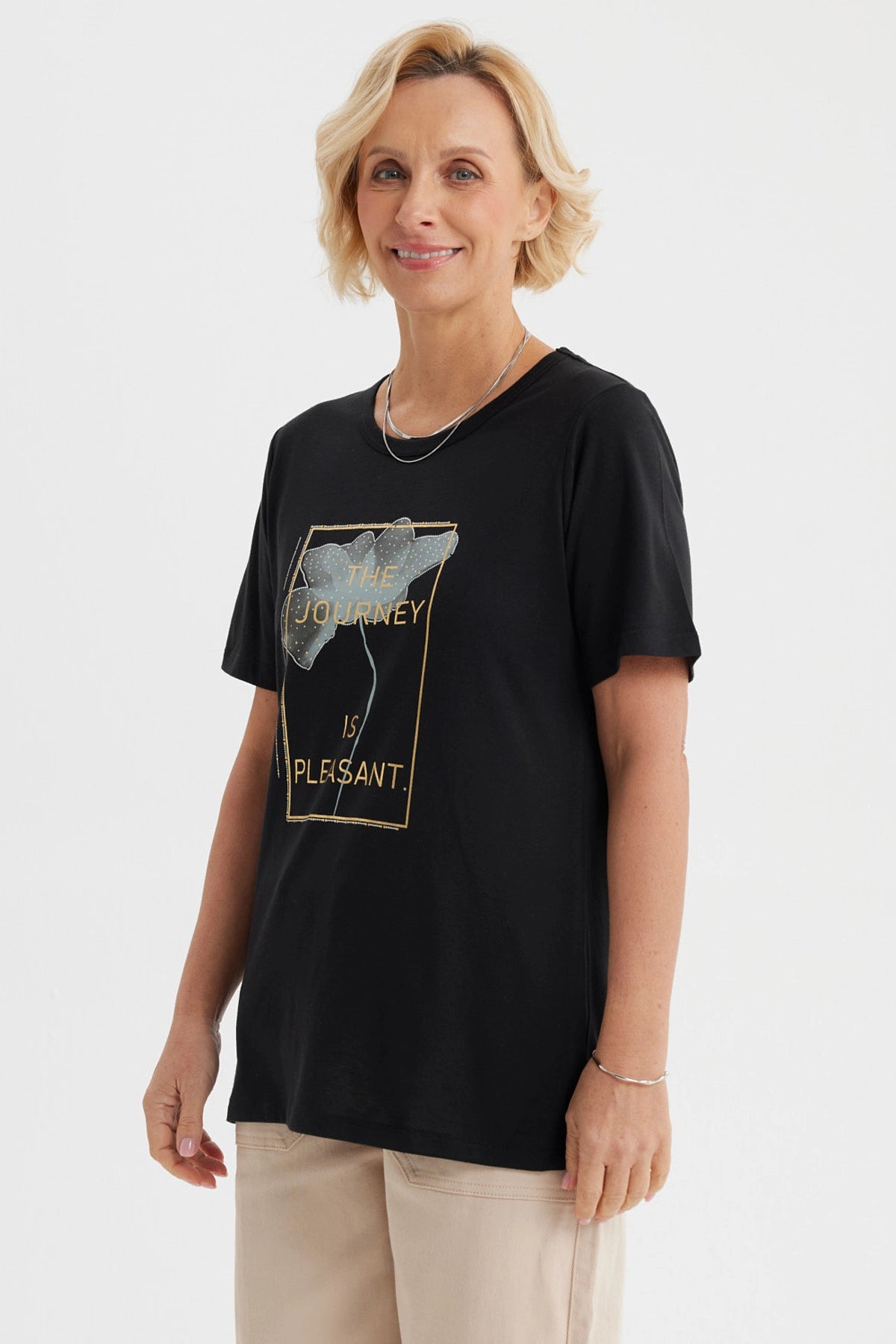 Polera negra mujer con estampado frontal de flor y texto The journey is pleasant en letras doradas