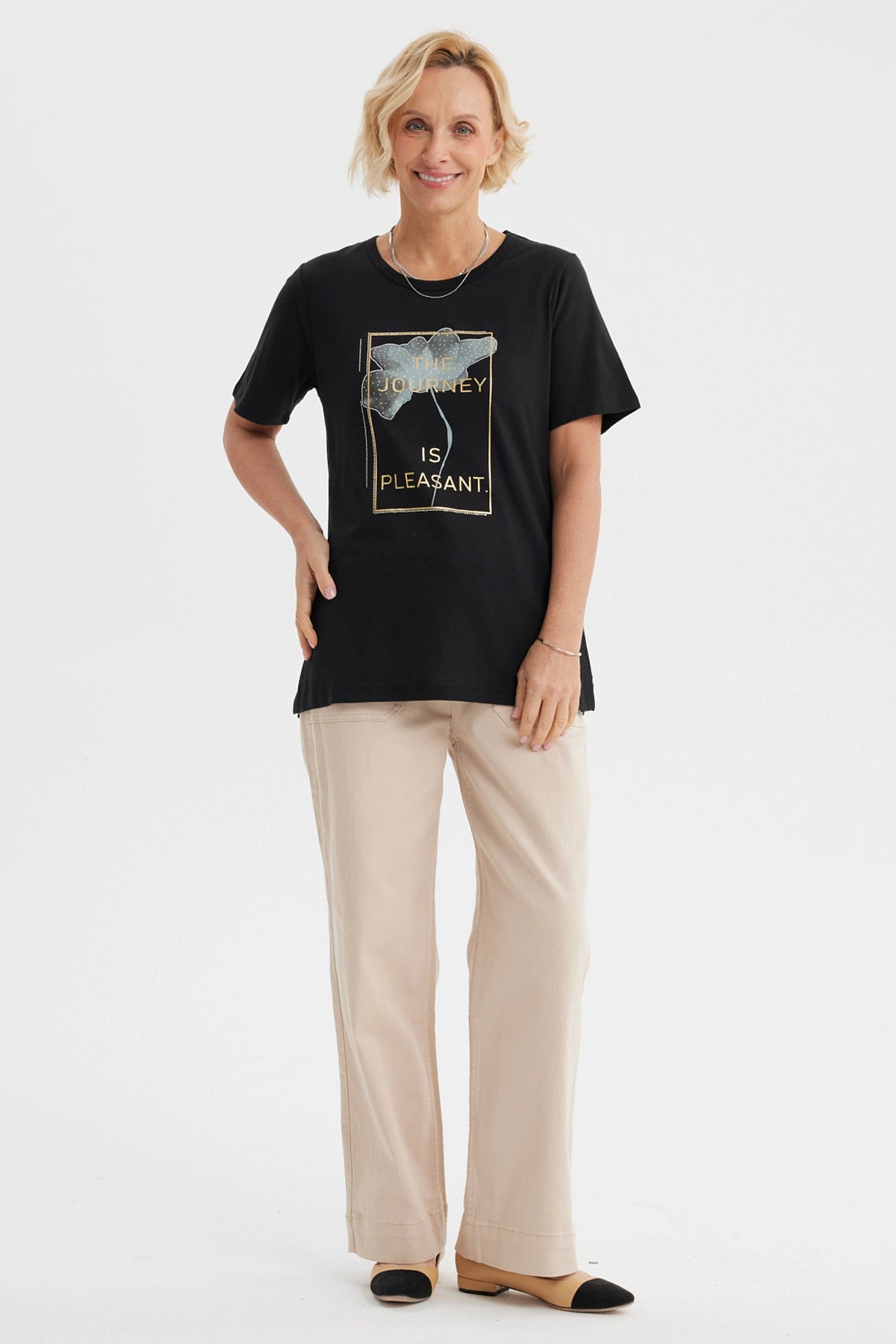 Polera negra mujer con estampado frontal de flor y texto The journey is pleasant en letras doradas
