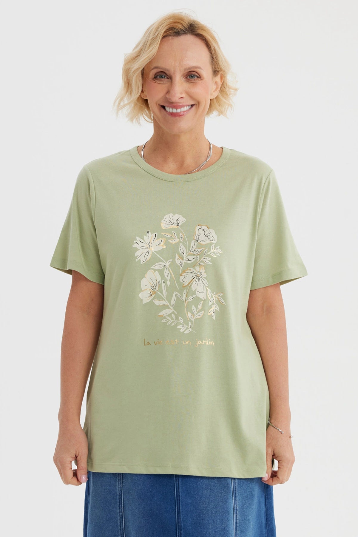Polera verde claro con estampado de flores blancas y texto La vie est un jardin al frente