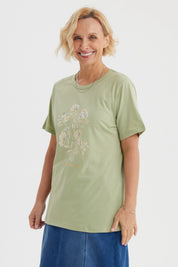 Polera verde claro con estampado de flores blancas y texto La vie est un jardin al frente