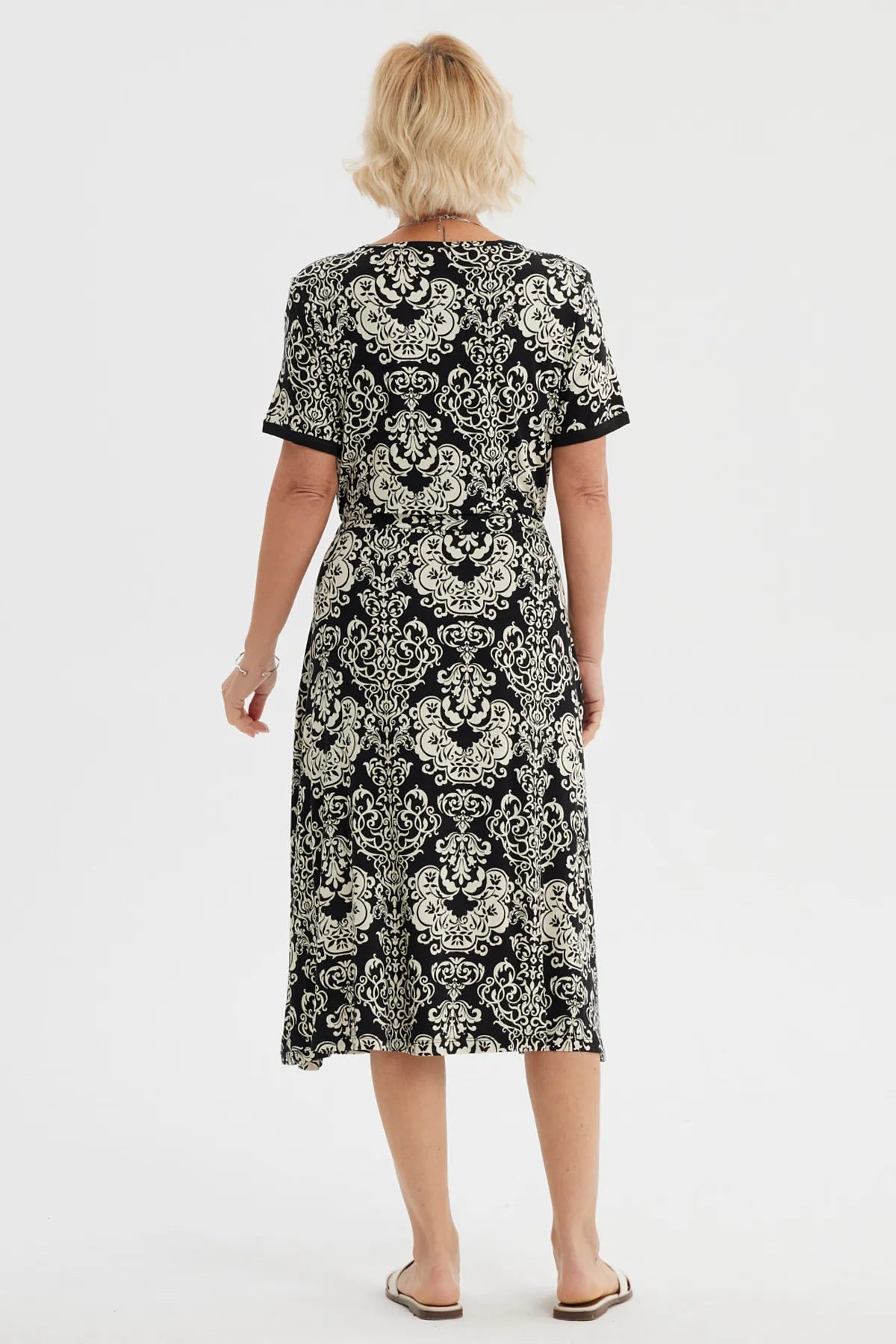 Vestido negro de mujer con estampado blanco de arabescos estilo vintage que cubre toda la prenda hasta las rodillas