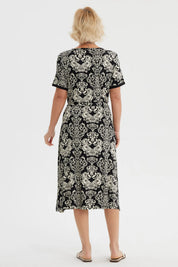 Vestido negro de mujer con estampado blanco de arabescos estilo vintage que cubre toda la prenda hasta las rodillas