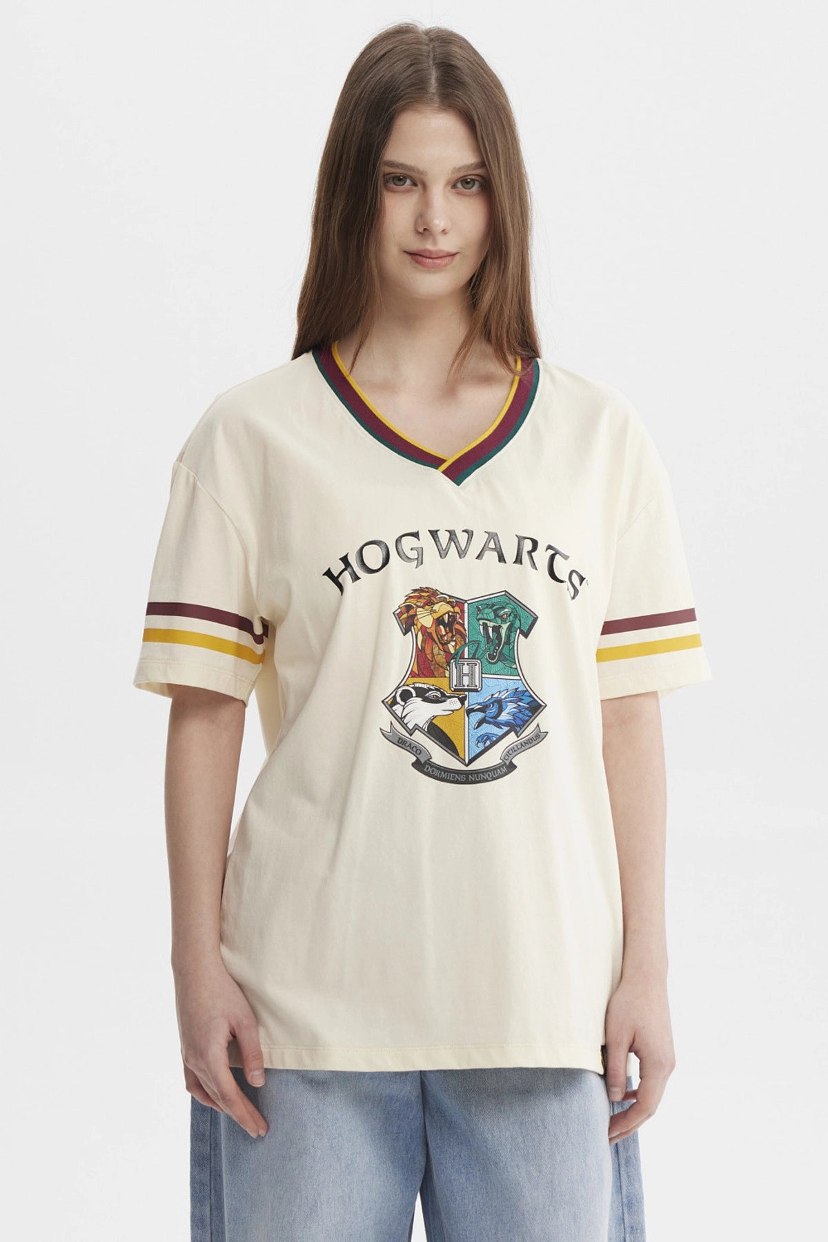 Polera beige de mujer con cuello en V y bordes a rayas con el escudo de Hogwarts grande en el centro estilo clásico