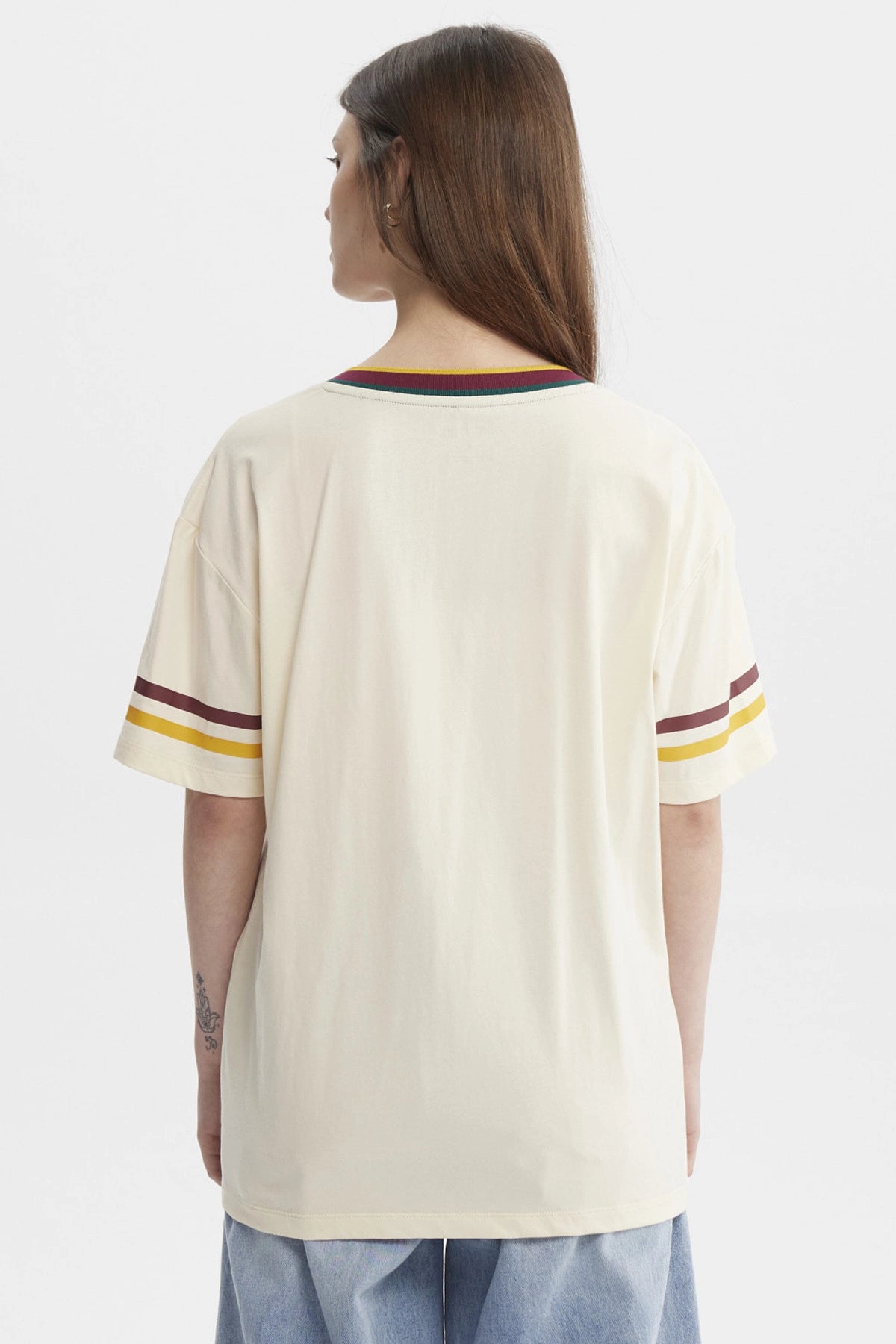 Polera beige de mujer con cuello en V y bordes a rayas con el escudo de Hogwarts grande en el centro estilo clásico