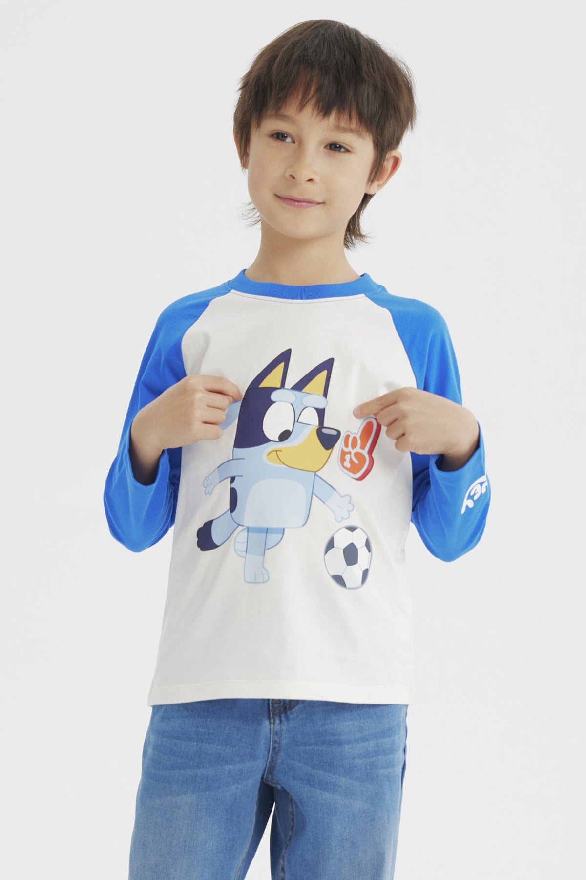 Polera crudo de niño con mangas azules y estampa de Bluey jugando fútbol al frente en estilo animado