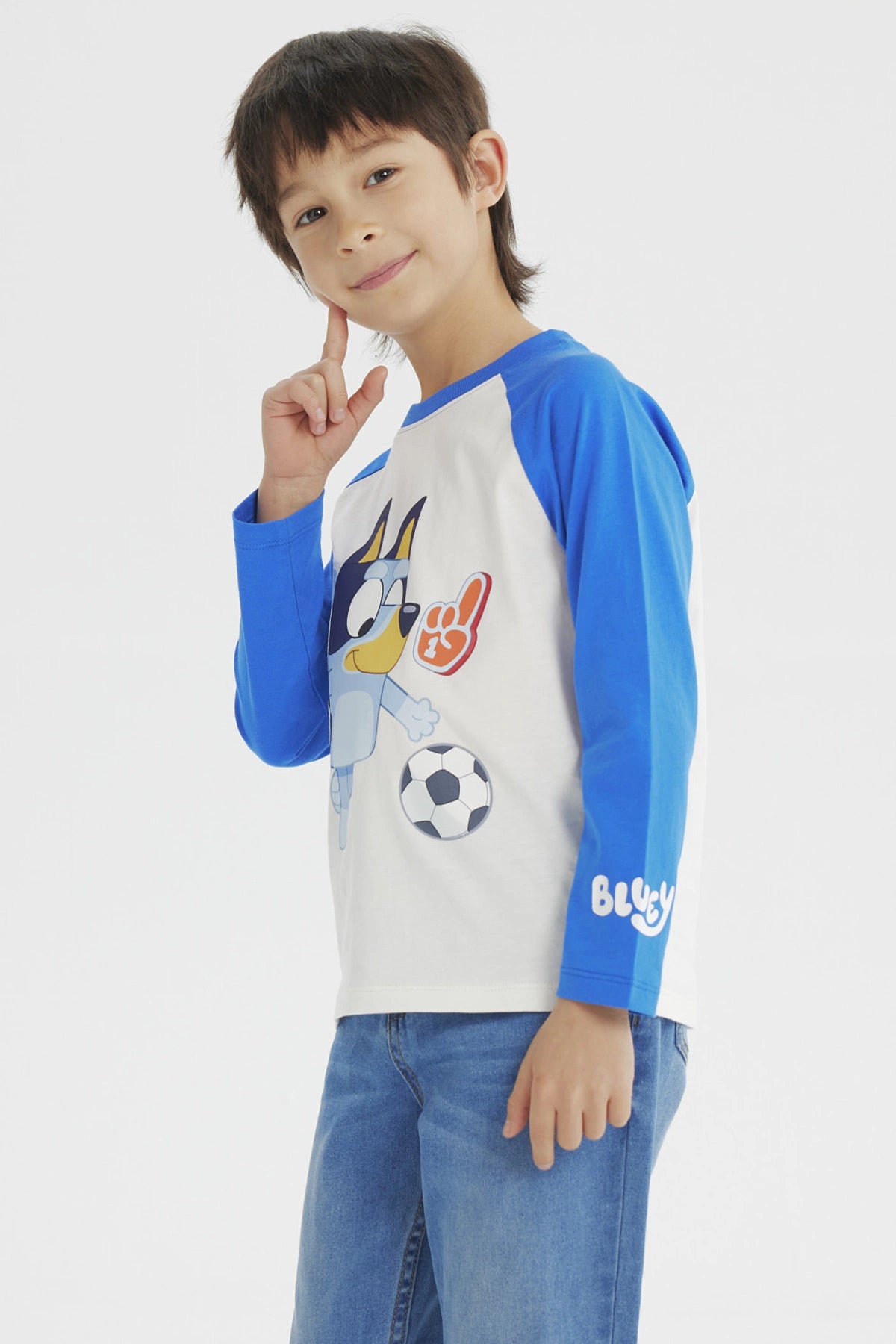 Polera crudo de niño con mangas azules y estampa de Bluey jugando fútbol al frente en estilo animado