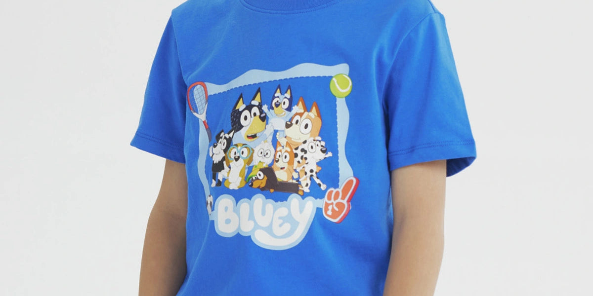 Polera azul para niño con estampa central de Bluey y amigos en un marco azul rodeado de pelotas y raquetas estilo dibujo animado