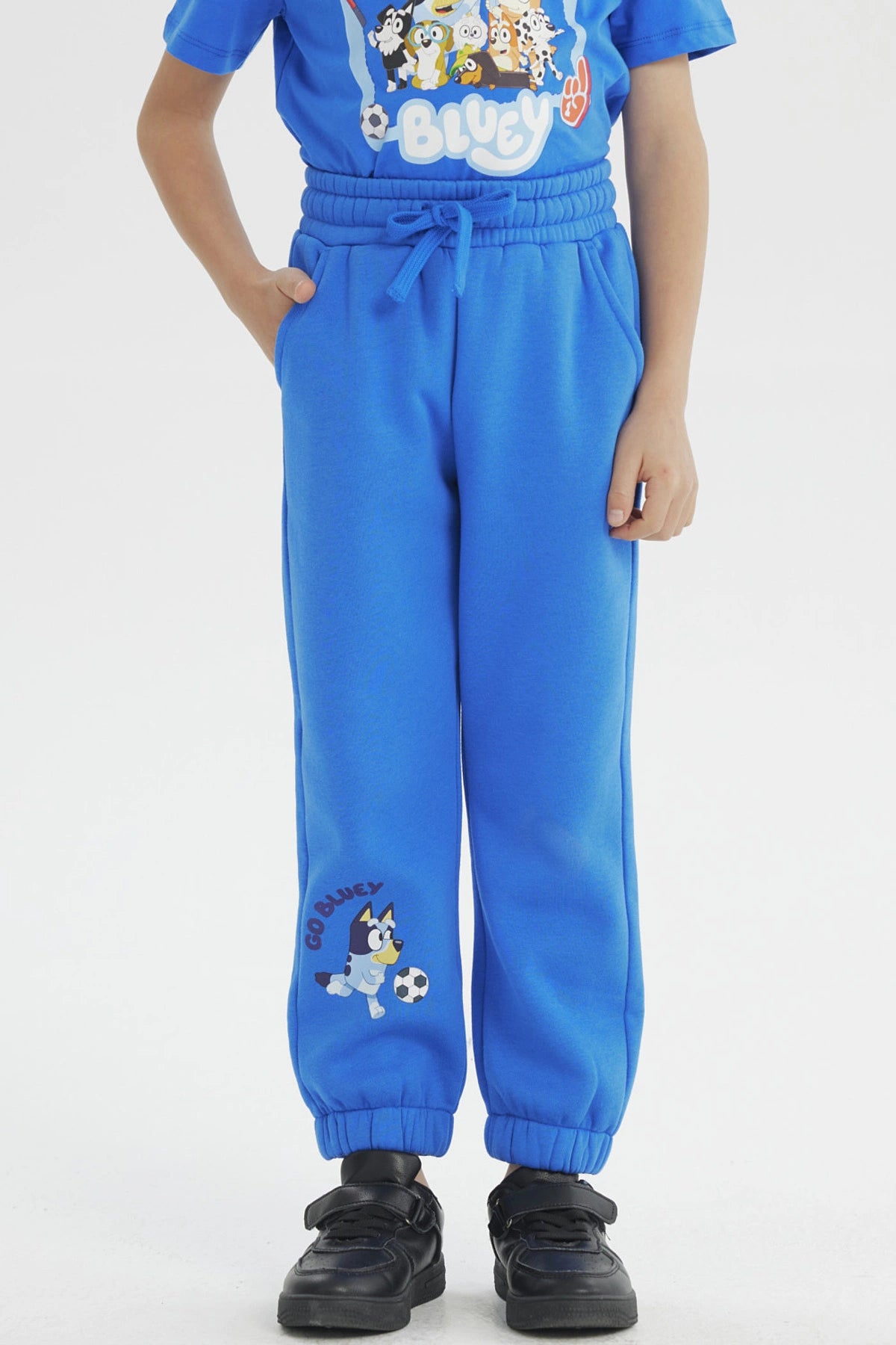 Pantalón buzo azul con diseño de Bluey jugando fútbol en la pierna izquierda de estilo infantil divertido