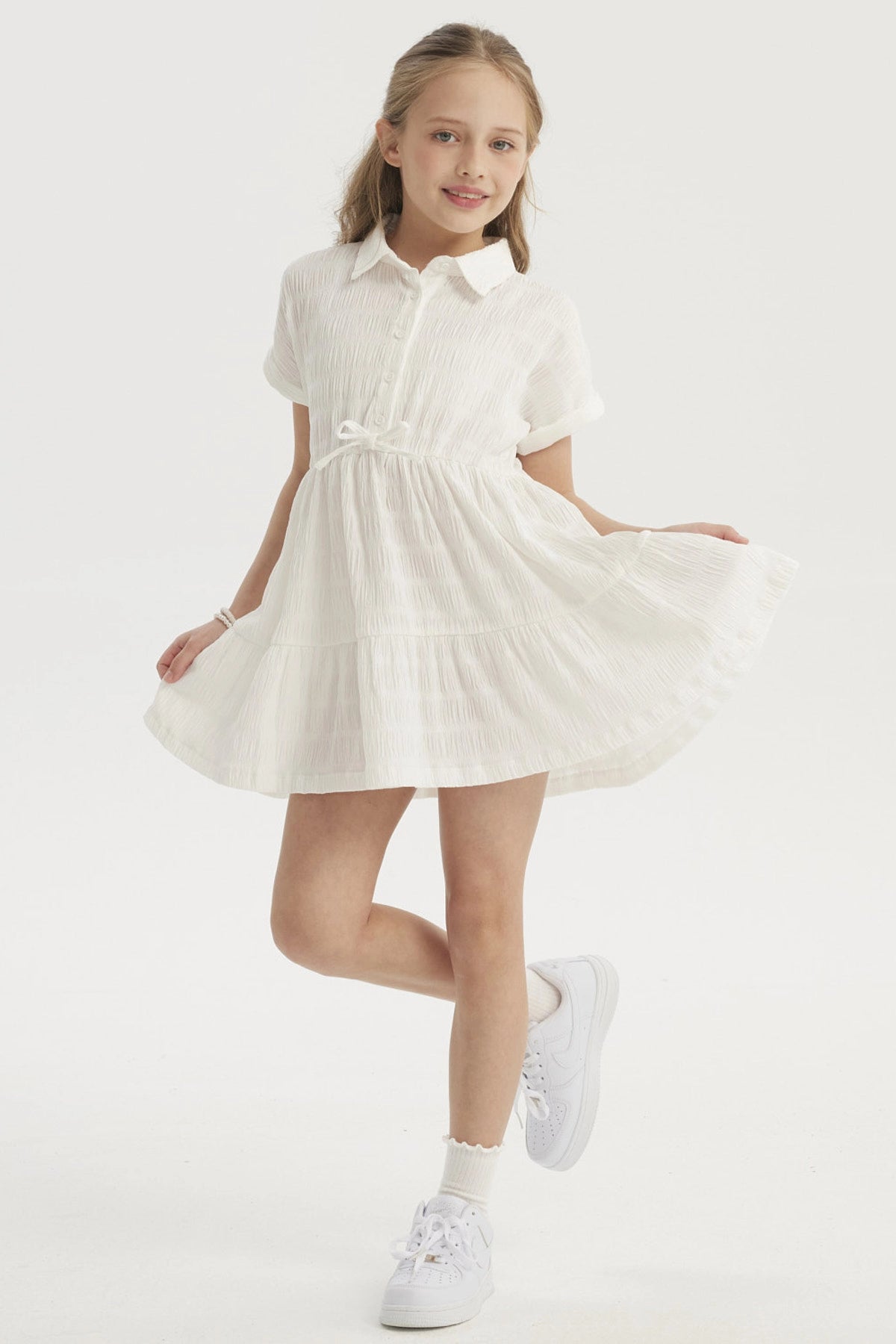 Vestido niña crudo con cuello redondo y mangas cortas detalle de lazo en cintura y diseño plisado liso