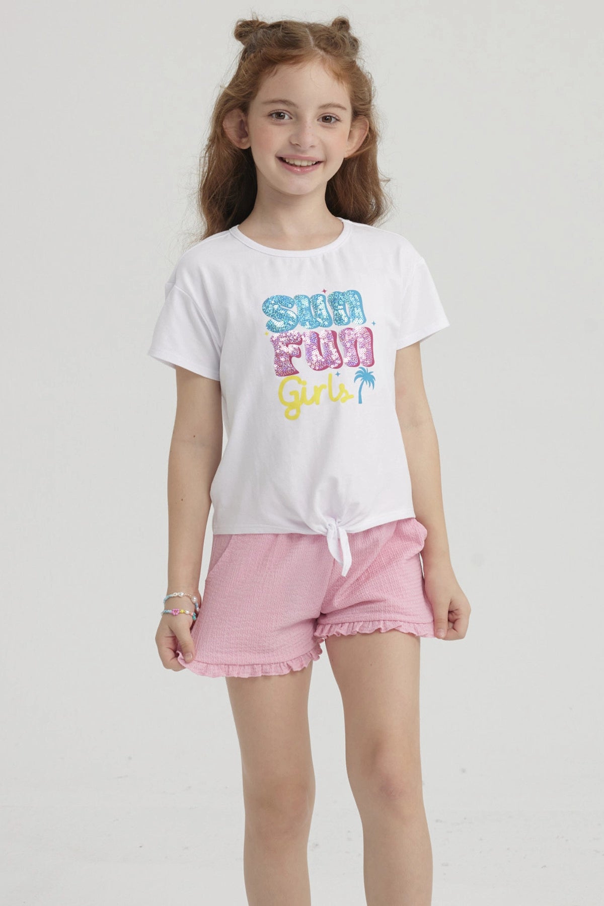 Polera blanca de niña con nudo frontal y estampado colorido que dice Sun Fun Girls con palmera pequeña al lado derecho
