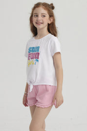 Polera blanca de niña con nudo frontal y estampado colorido que dice Sun Fun Girls con palmera pequeña al lado derecho