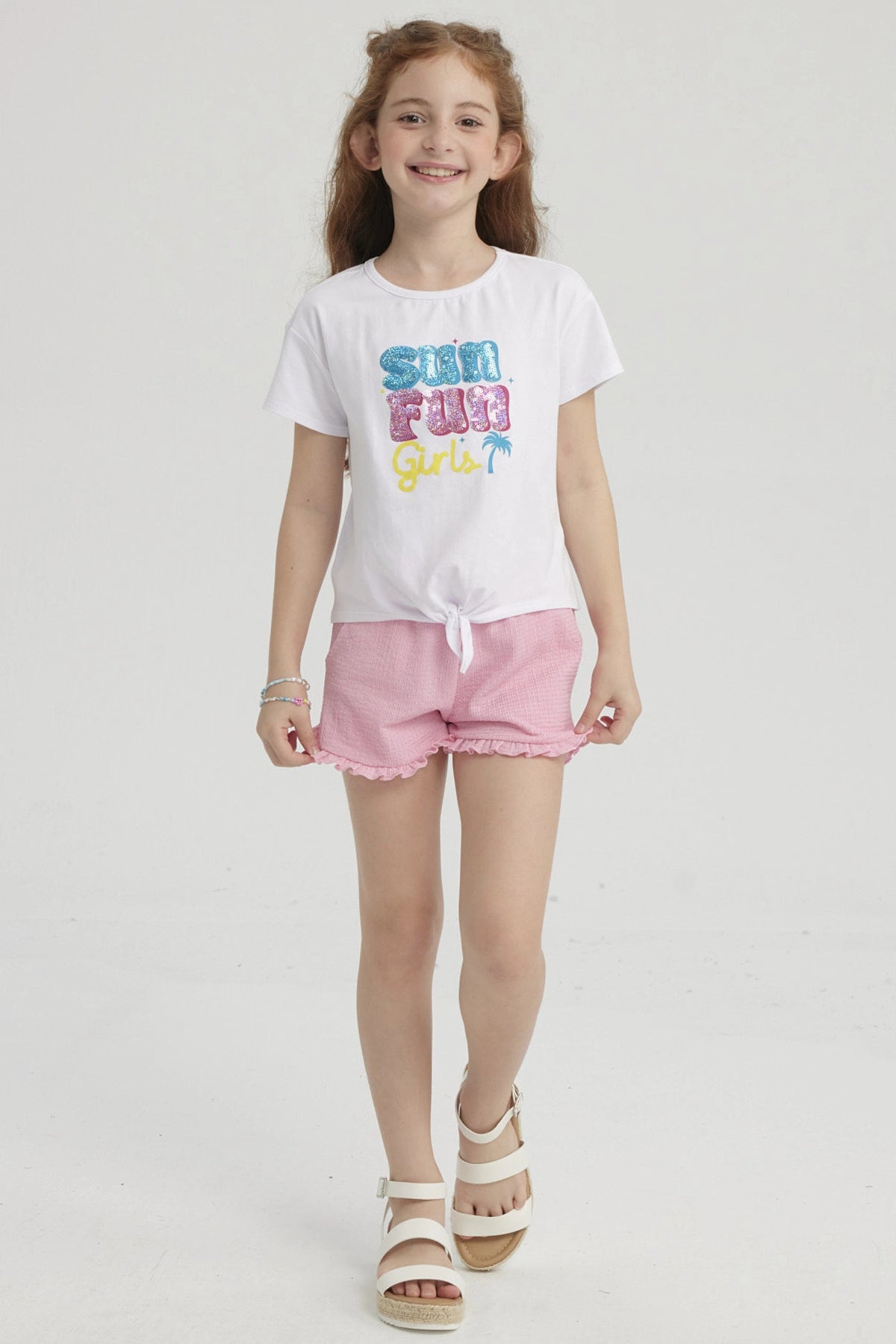Polera blanca de niña con nudo frontal y estampado colorido que dice Sun Fun Girls con palmera pequeña al lado derecho