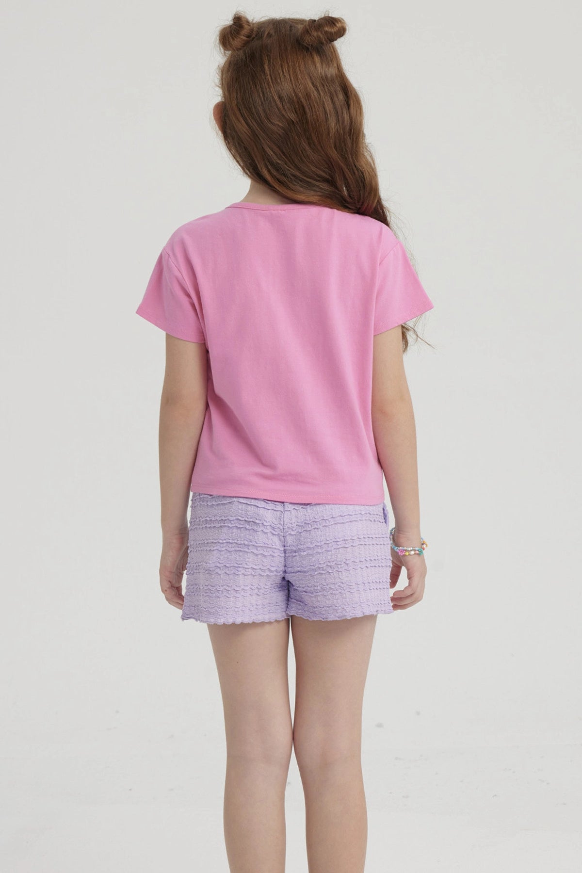 Polera rosada para niña con nudo al frente y estampado de piñas doradas pequeñas distribuidas por toda la prenda