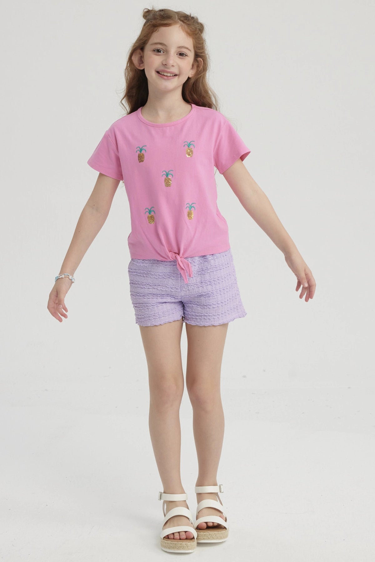 Polera rosada para niña con nudo al frente y estampado de piñas doradas pequeñas distribuidas por toda la prenda