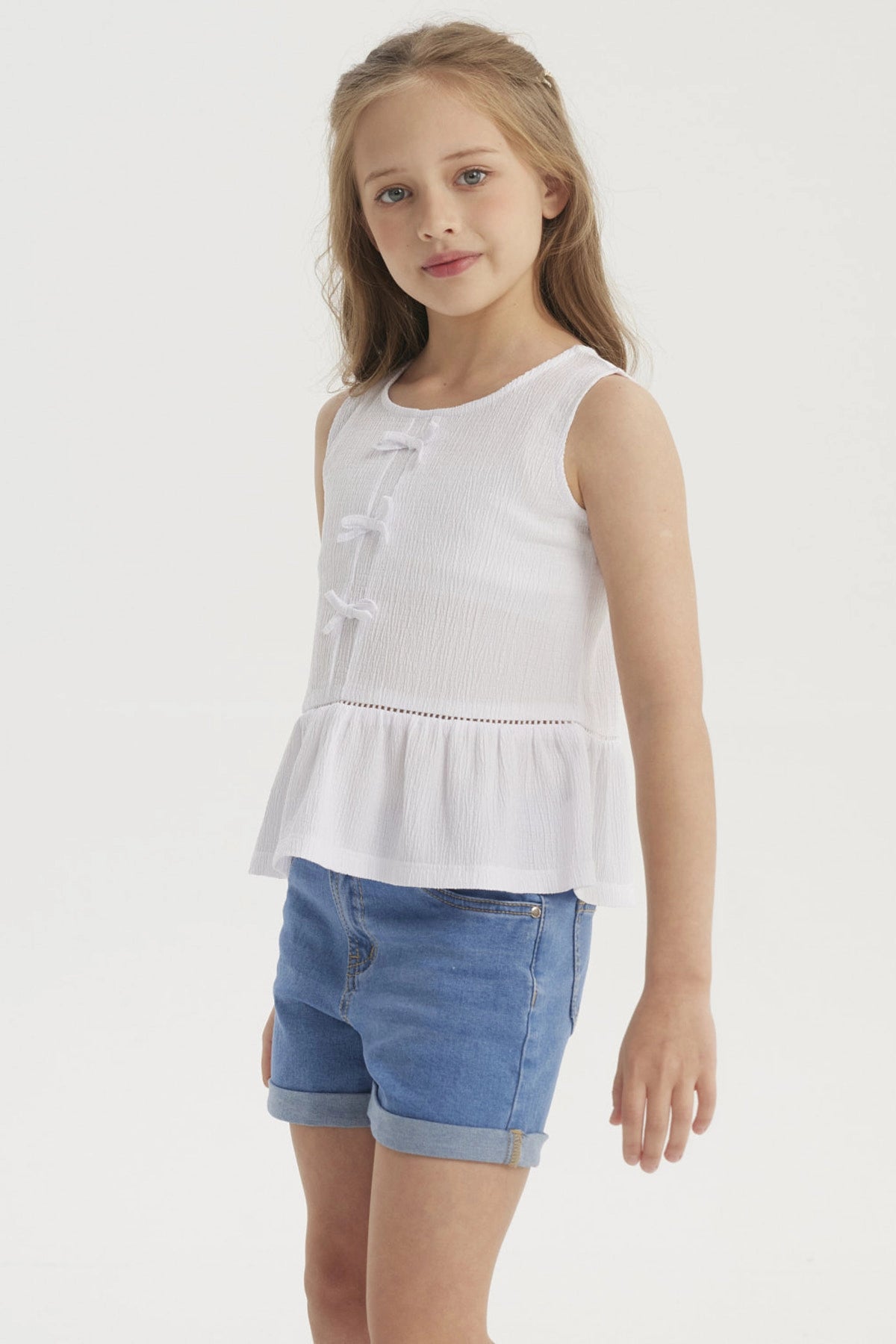 Polera blanca sin mangas para niña con cintas decorativas al frente y volante en el dobladillo diseño liso y elegante