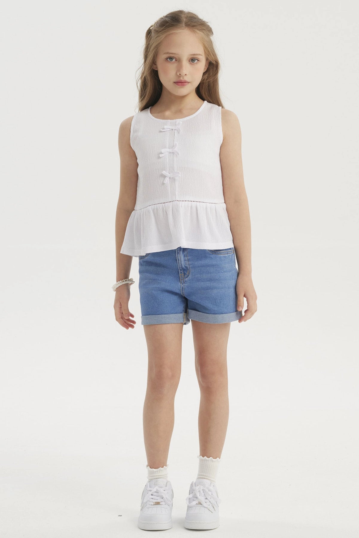 Polera blanca sin mangas para niña con cintas decorativas al frente y volante en el dobladillo diseño liso y elegante