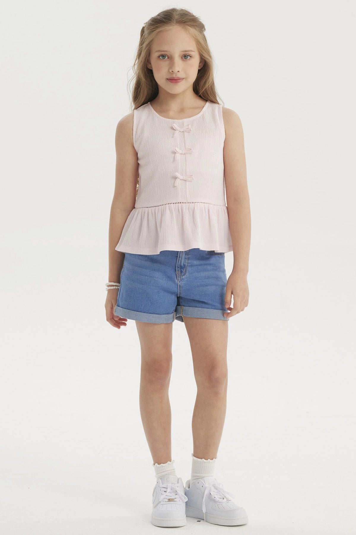 Polera niña rosada sin mangas con cintas decorativas en el frente y volantes en la cintura diseño liso