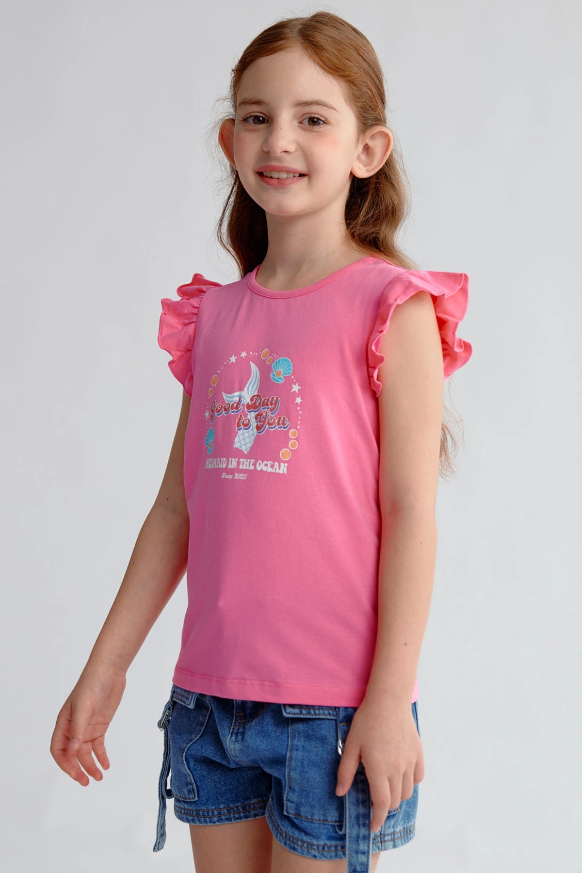 Polera niña fucsia con vuelos y diseño de conchas marinas en el frente