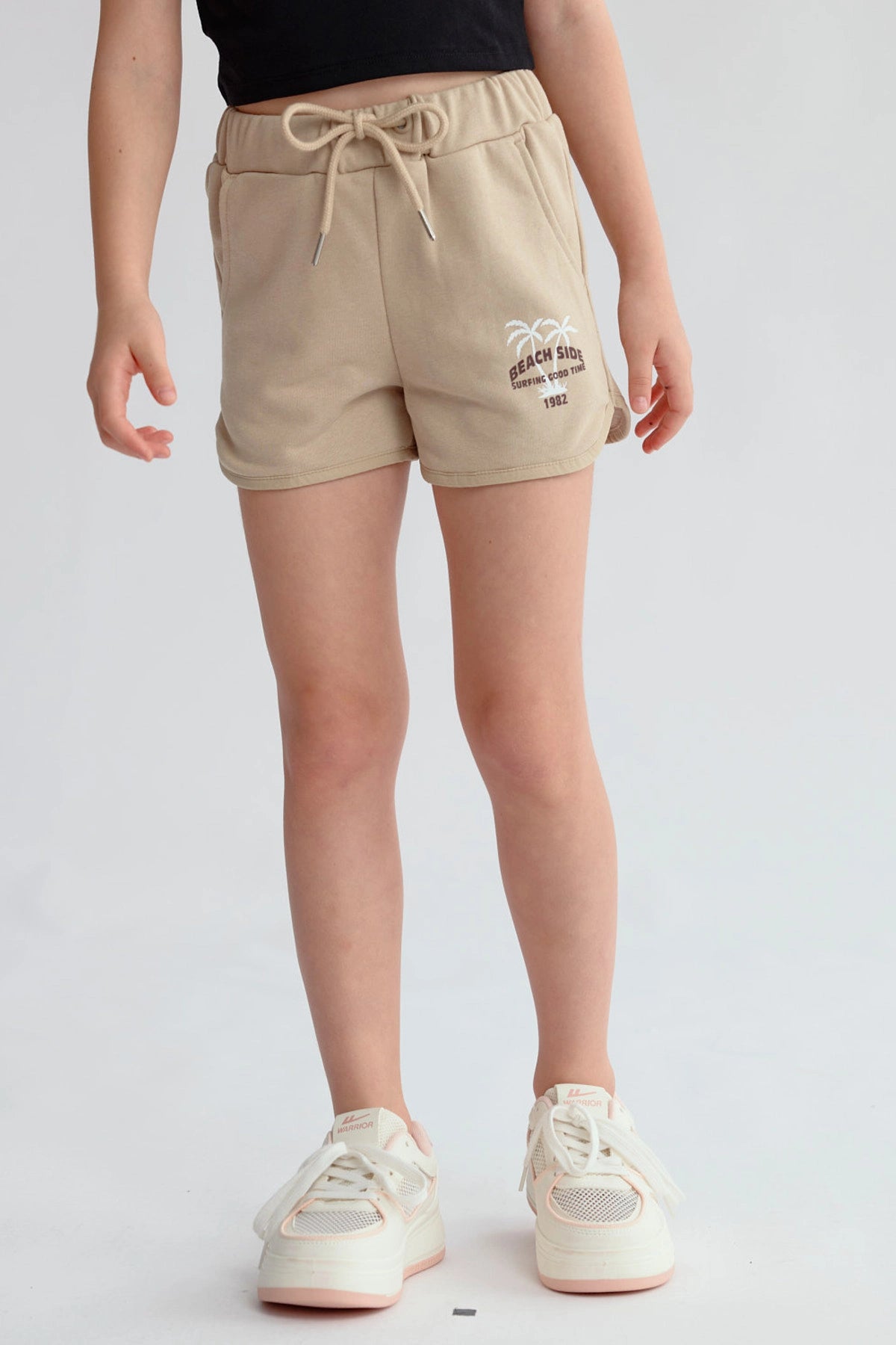 Short beige para niña con estampado de palmeras y texto en la pierna izquierda