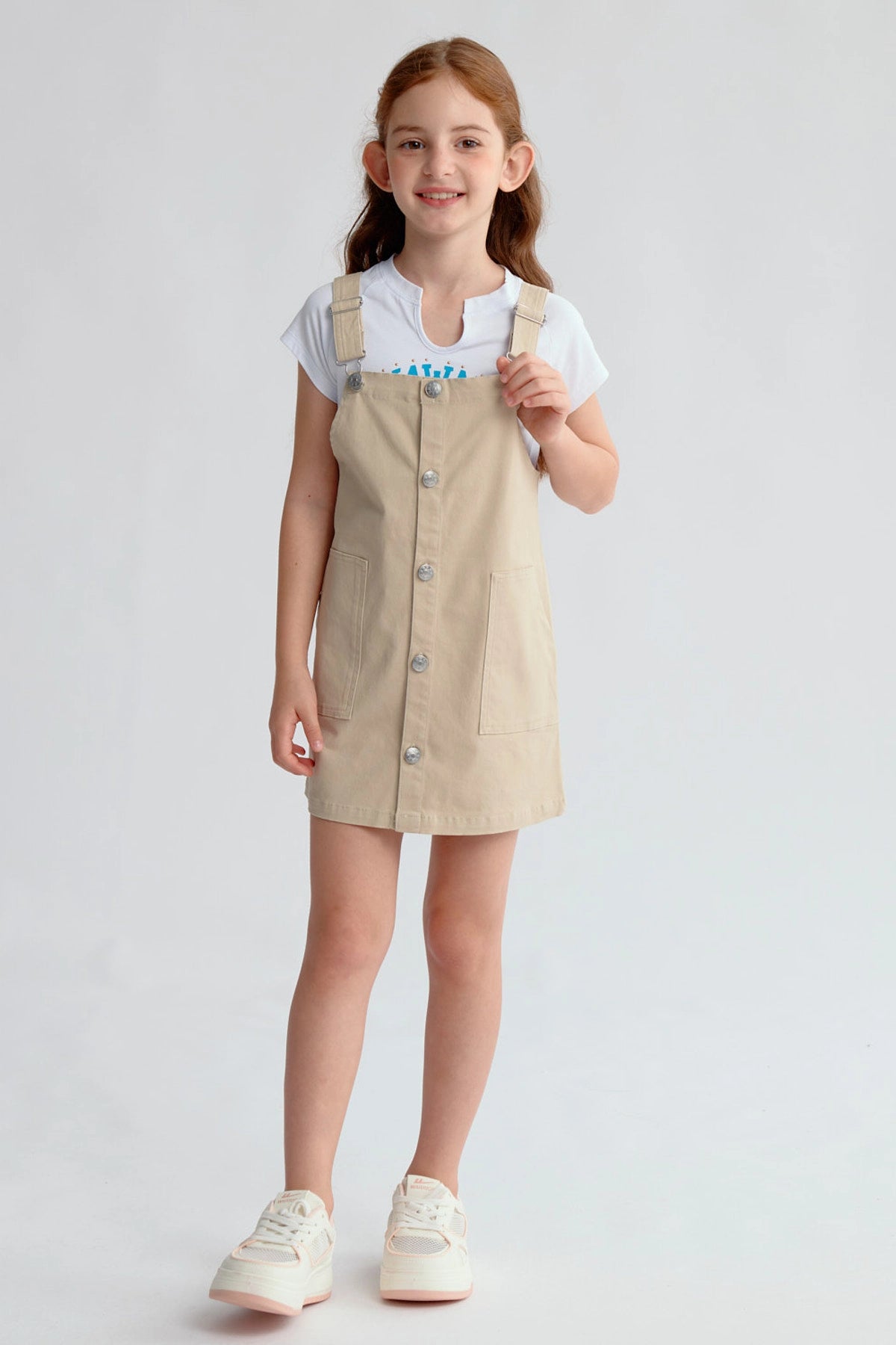 Jardinera tipo vestido beige para niña con botones frontales y bolsillos visibles