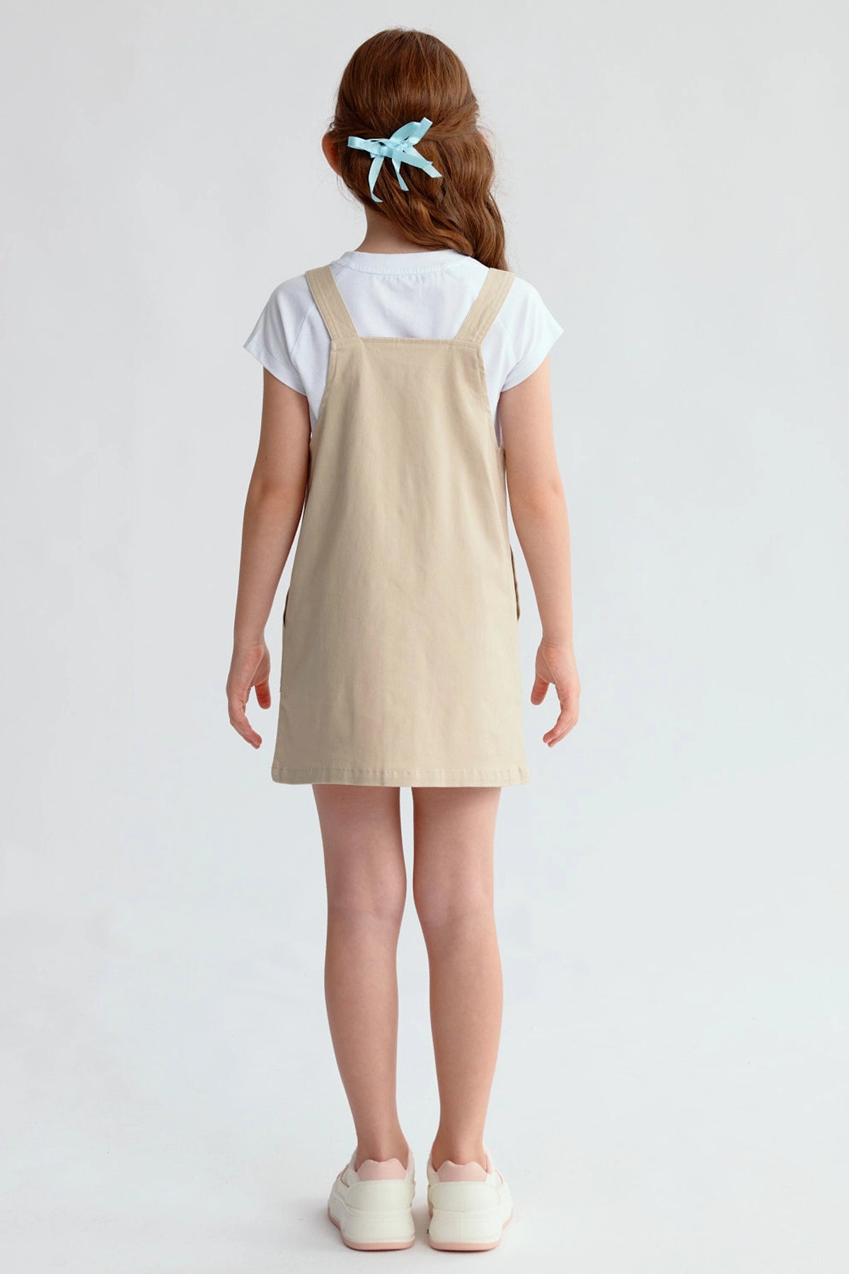 Jardinera tipo vestido beige para niña con botones frontales y bolsillos visibles