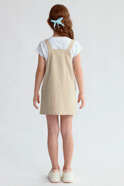 Jardinera tipo vestido beige para niña con botones frontales y bolsillos visibles