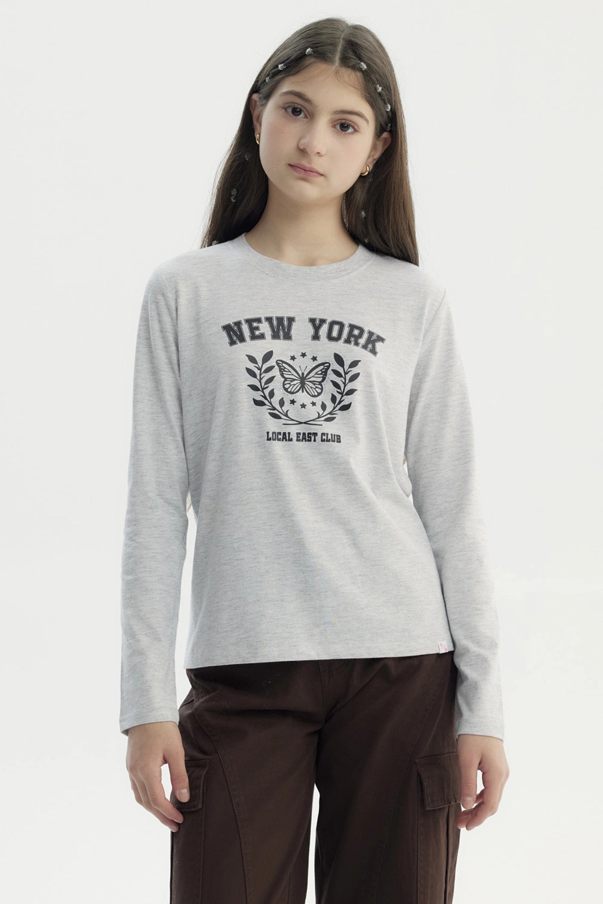 Polera niña gris melange con estampa central de mariposa y texto New York Local East Club en estilo universitario