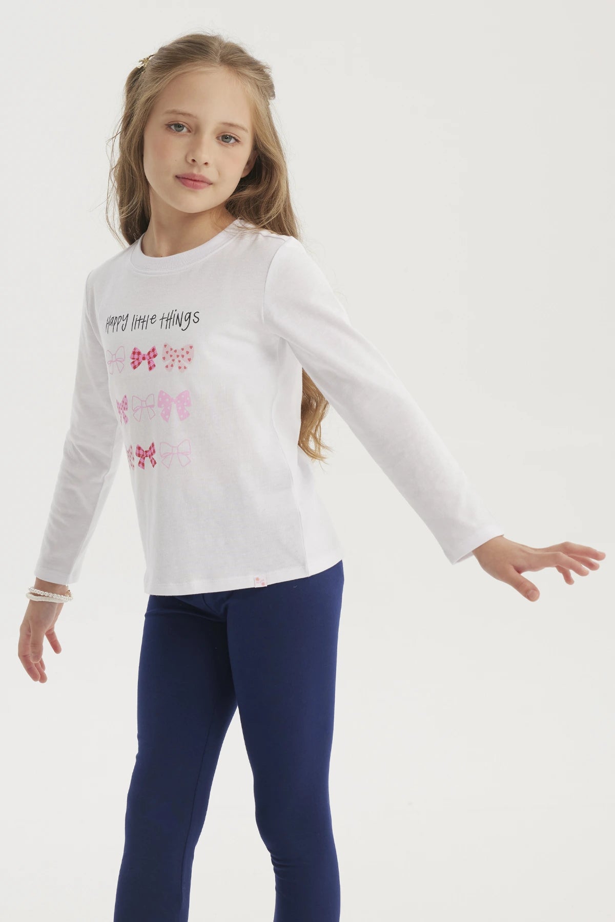 Polera blanca de niña con estampado de lazos en colores rosados y rojos en el centro con texto Happy little things