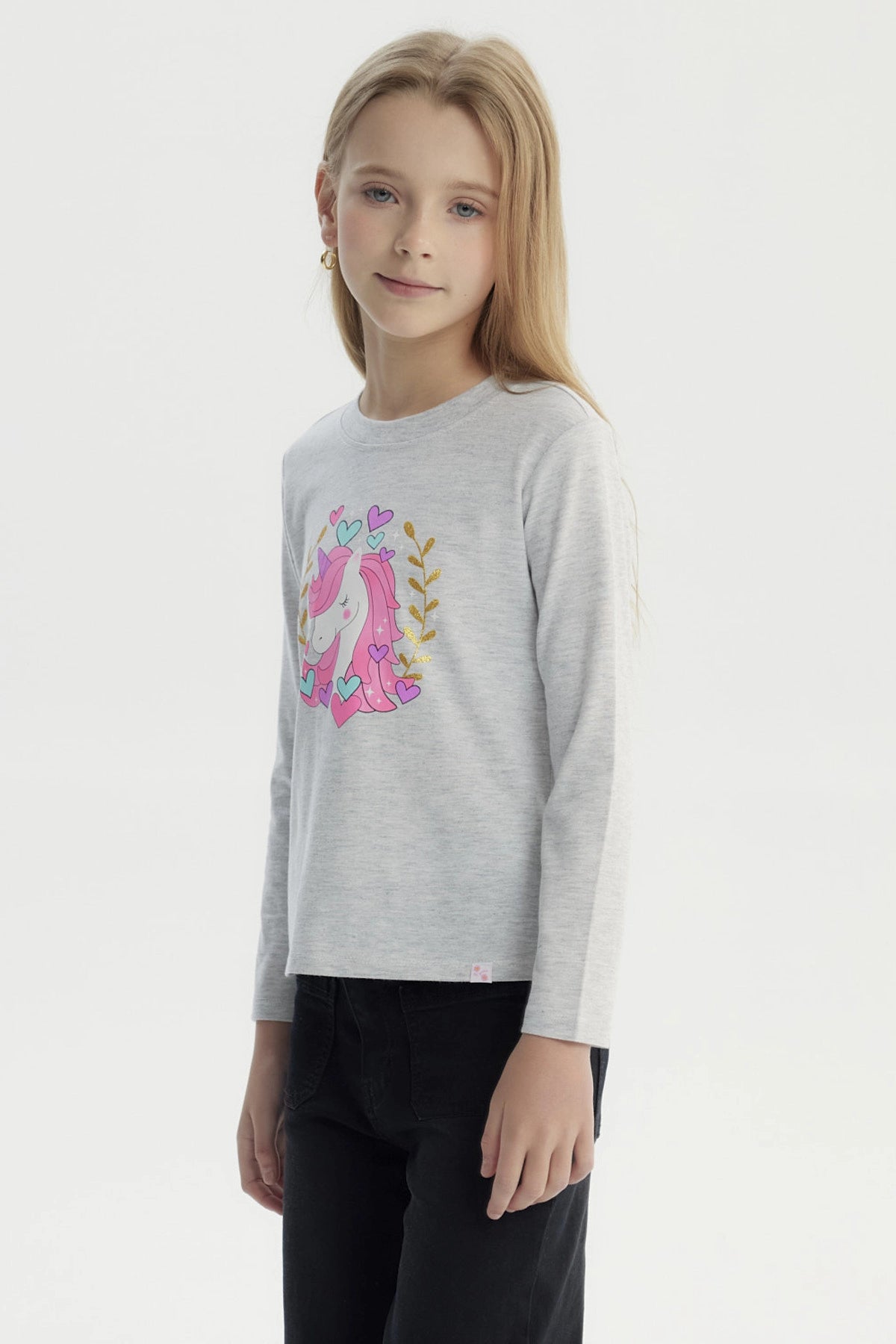 Polera gris melange de niña con estampa central de unicornio rosado rodeado de corazones y hojas doradas estilo dibujo