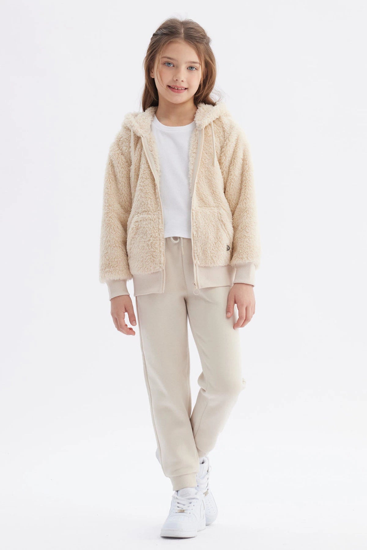 Polar niña beige con capucha y textura peluda cierre frontal y bolsillos delanteros diseño liso cómodo y abrigador