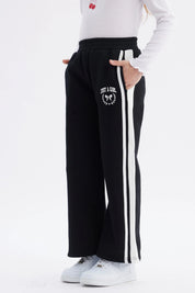 Pantalón buzo niña negro con pierna ancha y franjas blancas Just a Girl en el muslo diseño casual y cómodo