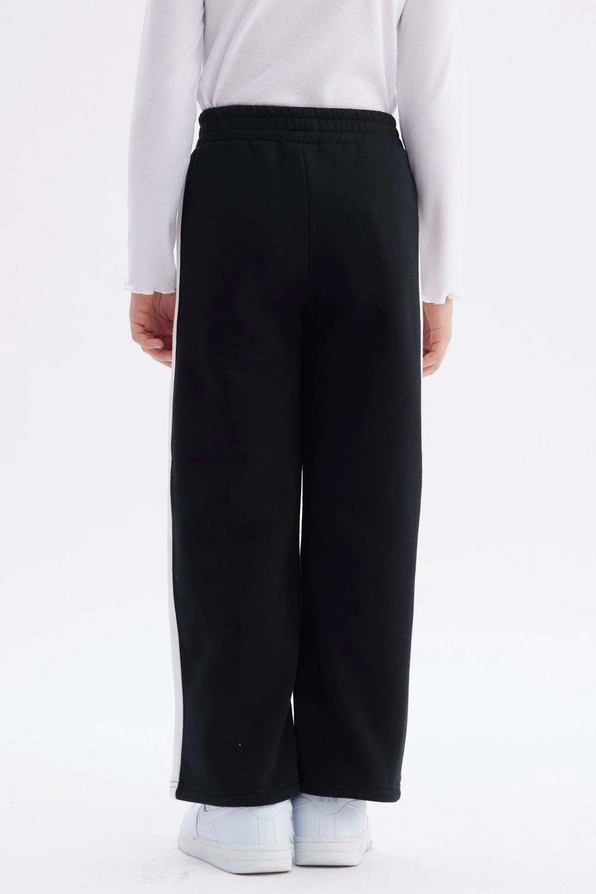 Pantalón buzo niña negro con pierna ancha y franjas blancas Just a Girl en el muslo diseño casual y cómodo