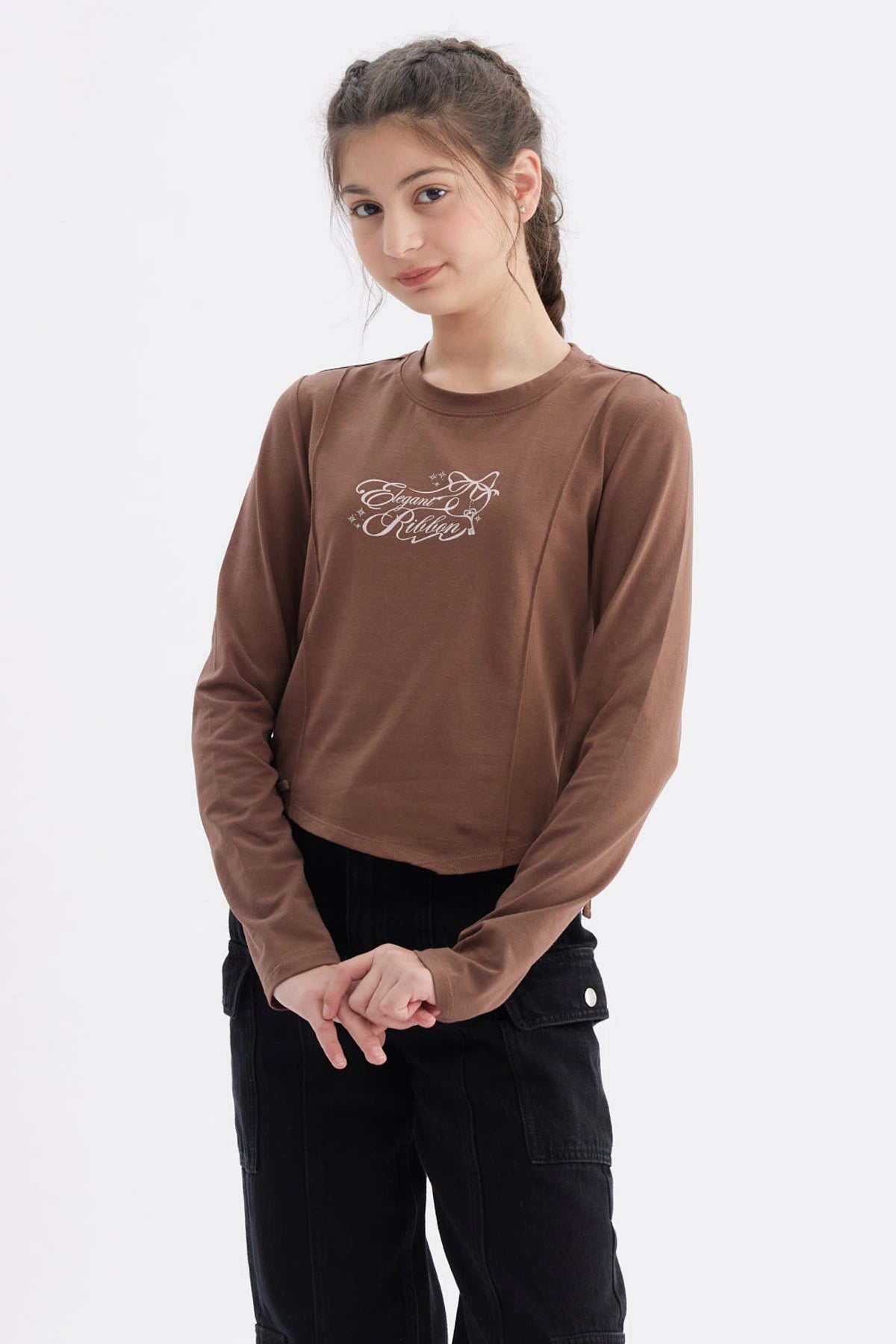Polera niña slim café con diseño frontal de texto 'Elegant Ribbon' en estilo cursivo centrado sobre el pecho