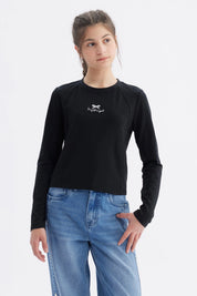 Polera negra de manga larga para niña con estampa de moño y texto I'm just a girl en el centro del pecho