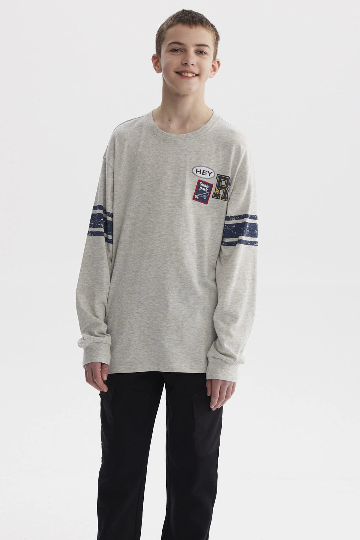 Polera gris melange de niño con franjas azules en mangas y parches tipo college en el pecho estilo casual urbano