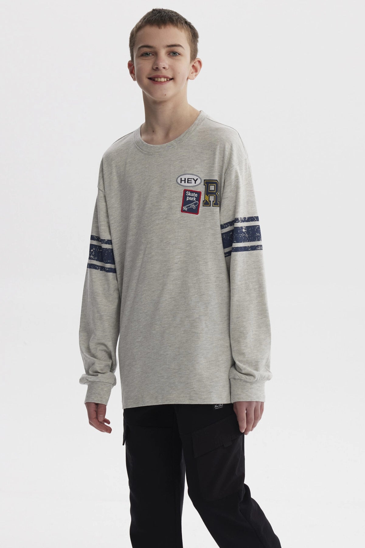 Polera gris melange de niño con franjas azules en mangas y parches tipo college en el pecho estilo casual urbano