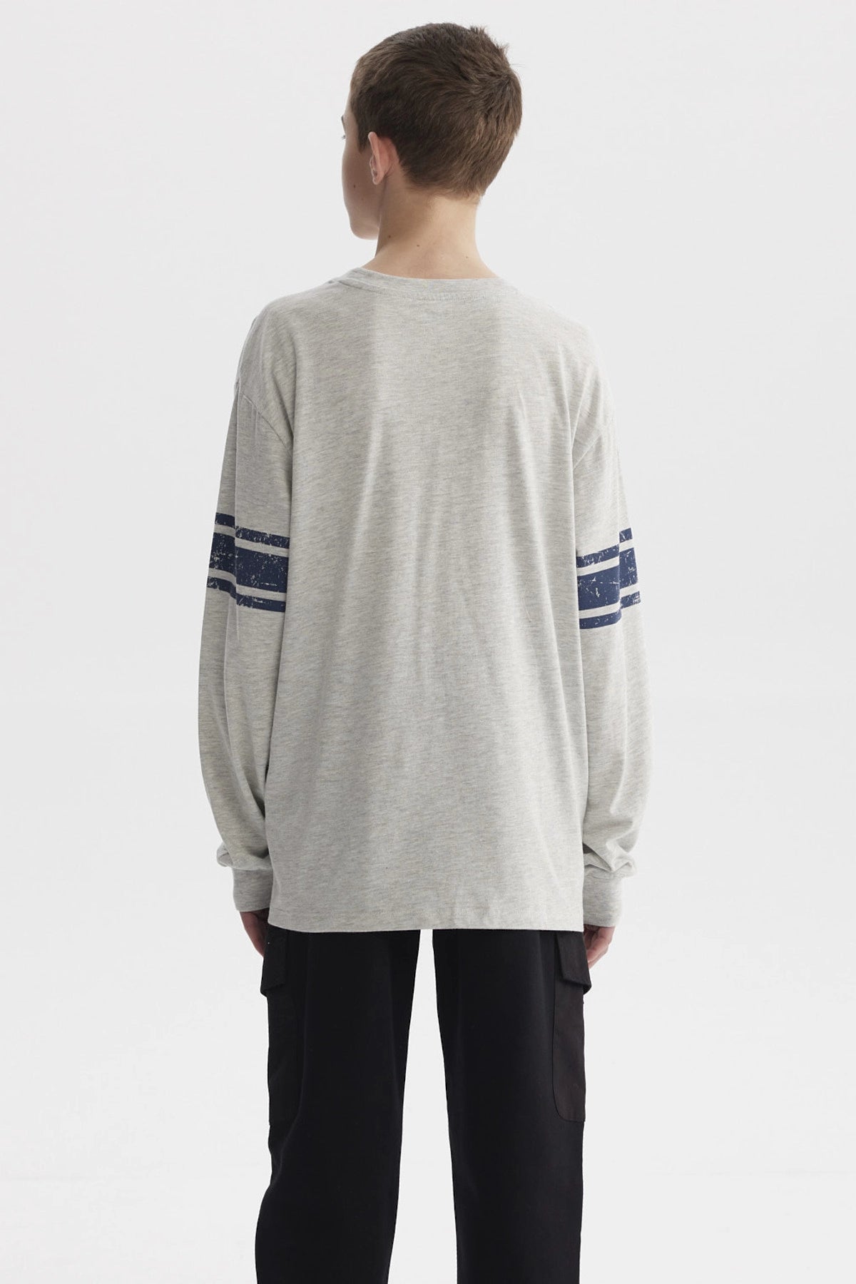 Polera gris melange de niño con franjas azules en mangas y parches tipo college en el pecho estilo casual urbano