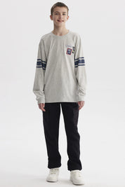 Polera gris melange de niño con franjas azules en mangas y parches tipo college en el pecho estilo casual urbano
