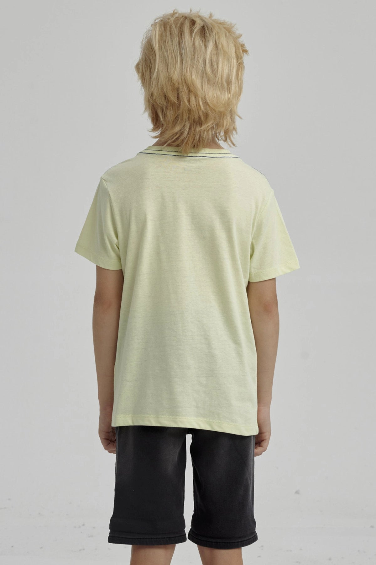 Polera amarilla para niño con bolsillo y estampa de esqueleto surfeando en estilo gráfico pequeño sobre el pecho