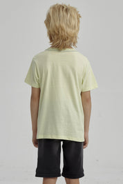 Polera amarilla para niño con bolsillo y estampa de esqueleto surfeando en estilo gráfico pequeño sobre el pecho