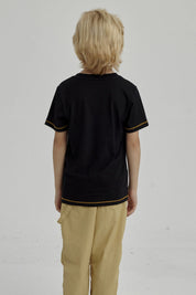 Polera negra para niño con diseño de dinosaurio surfeando y texto Surf Calling en el pecho estilo gráfico amarillo