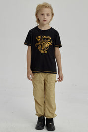 Polera negra para niño con diseño de dinosaurio surfeando y texto Surf Calling en el pecho estilo gráfico amarillo